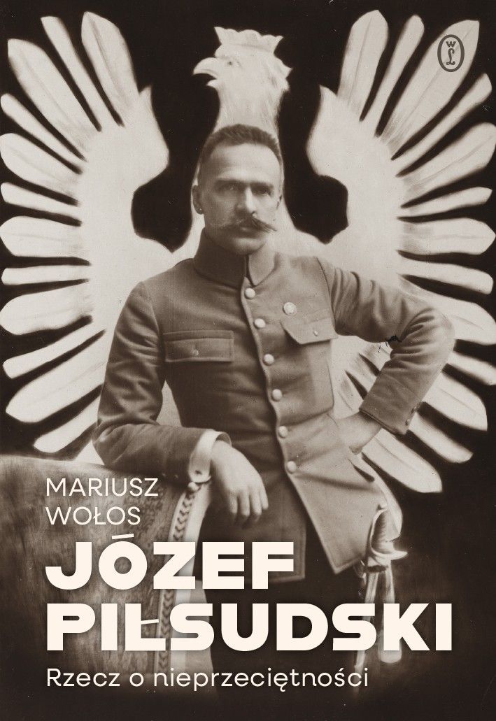 Opis okładki książki „Józef Piłsudski. Rzecz o nieprzeciętności” – Mariusz Wołos Okładka utrzymana jest w tonacji sepii, nadającej jej historyczny i poważny charakter. Centralnym elementem jest fotografia mężczyzny w mundurze wojskowym, siedzącego w pewnej, pewnej siebie pozie. Za nim widnieje duży, jasny wizerunek stylizowanego orła z rozpostartymi skrzydłami — symbolu narodowego. Na dole okładki, wyraźną, dużą i nowoczesną czcionką zapisano tytuł: JÓZEF PIŁSUDSKI Rzecz o nieprzeciętności Wyżej, po lewej stronie, znajduje się nazwisko autora: Mariusz Wołos. W prawym górnym rogu widnieje znak wydawnictwa Wydawnictwo Literackie. Całość łączy atmosferę historycznej powagi z czytelnym, współczesnym designem, podkreślając wyjątkowość postaci będącej tematem książki.