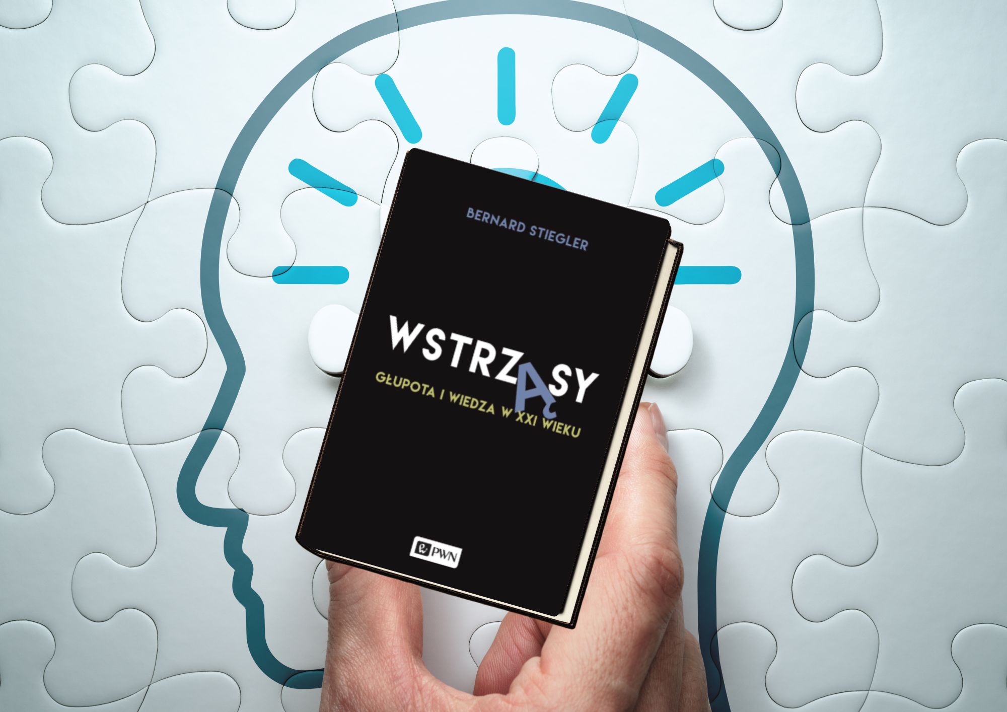 Na grafice widoczna jest książka „Wstrząsy. Głupota i wiedza w XXI wieku” autorstwa Bernarda Stieglera, wydana przez PWN. Okładka samej książki jest czarna, minimalistyczna i elegancka. Tytuł „WSTRZĄSY” zapisany jest dużą, białą czcionką, z wyróżnioną literą „Ą” w niebieskim kolorze, co stanowi subtelny akcent graficzny. Podtytuł „Głupota i wiedza w XXI wieku” zapisano mniejszą, żółtą czcionką, co tworzy kontrast i podkreśla intelektualny, eseistyczno-filozoficzny charakter publikacji. Książka trzymana jest w dłoni, a tło stanowi jasna kompozycja złożona z elementów puzzli. Linie puzzli układają się w zarys ludzkiej głowy, wokół której widoczne są turkusowe promienie przypominające symbole idei lub przebłysku myśli. Motyw ten można interpretować jako metaforę myślenia, wiedzy, świadomości oraz złożoności współczesnego świata. Całość tworzy spójną, symboliczną kompozycję – zestawienie czarnej, poważnej okładki z jasnym, „umysłowym” tłem podkreśla refleksyjny i krytyczny charakter książki.