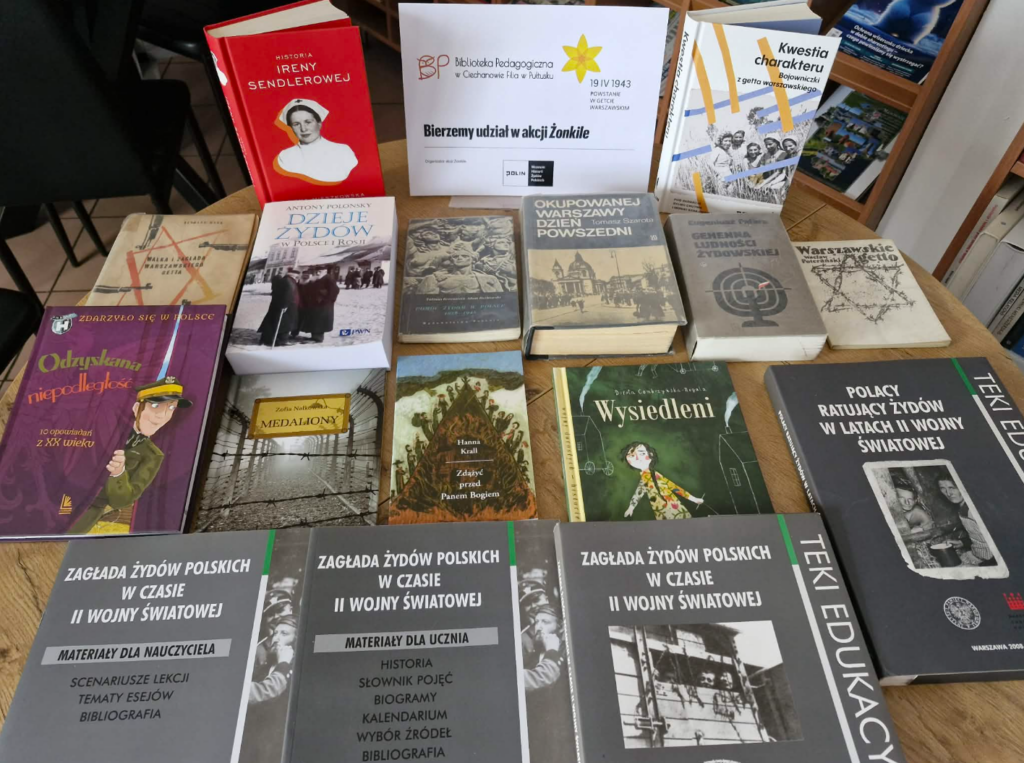 Na zdjęciu widoczna jest tematyczna ekspozycja książek przygotowana w bibliotece w związku z udziałem w akcji Żonkile.

Na środku ustawiono planszę informacyjną z napisem „Bierzemy udział w akcji Żonkile”, z logo Biblioteka Pedagogiczna w Ciechanowie Filia w Pułtusku oraz odniesieniem do rocznicy Powstanie w getcie warszawskim (19 IV 1943). Obok znajduje się informacja o organizatorze – Muzeum Historii Żydów Polskich POLIN.

Na stole rozłożono liczne książki o tematyce historycznej, dotyczące przede wszystkim losów Żydów w czasie II wojny światowej, Holokaustu oraz okupacji. Wśród nich można zauważyć m.in.:
biografię Ireny Sendlerowej,
publikacje o dziejach Żydów w Polsce,
książki o życiu w okupowanej Warszawie i getcie warszawskim,
literaturę dla dzieci i młodzieży (np. „Medaliony”, „Zdążyć przed Panem Bogiem”),
materiały edukacyjne dla nauczycieli i uczniów („Zagłada Żydów polskich w czasie II wojny światowej”).

Ekspozycja ma charakter edukacyjny i służy upowszechnianiu wiedzy o Holokaust oraz historii społeczności żydowskiej w Polsce. Całość została starannie ułożona, aby zachęcić czytelników do sięgania po literaturę i pogłębiania wiedzy historycznej.