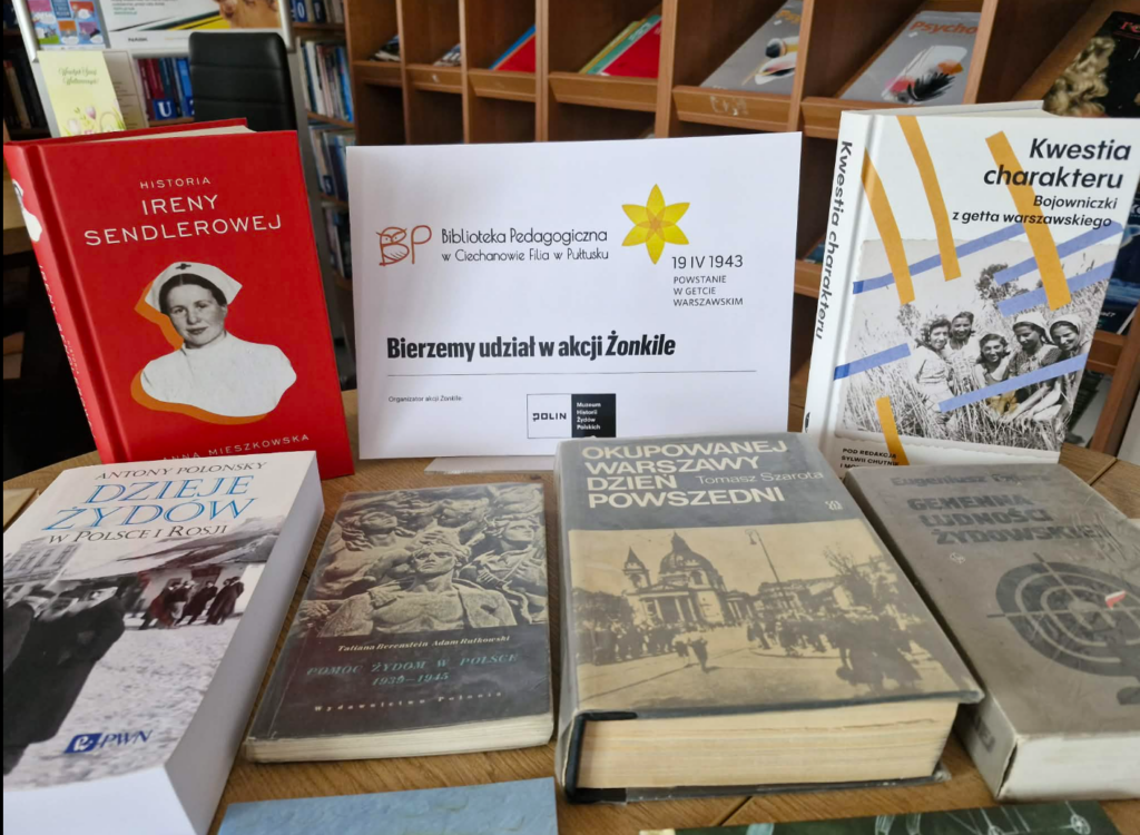 Na zdjęciu widoczna jest tematyczna ekspozycja książek przygotowana w bibliotece w związku z udziałem w akcji Żonkile.

Na środku ustawiono planszę informacyjną z napisem „Bierzemy udział w akcji Żonkile”, z logo Biblioteka Pedagogiczna w Ciechanowie Filia w Pułtusku oraz odniesieniem do rocznicy Powstanie w getcie warszawskim (19 IV 1943). Obok znajduje się informacja o organizatorze – Muzeum Historii Żydów Polskich POLIN.

Na stole rozłożono liczne książki o tematyce historycznej, dotyczące przede wszystkim losów Żydów w czasie II wojny światowej, Holokaustu oraz okupacji. Wśród nich można zauważyć m.in.:
biografię Ireny Sendlerowej,
publikacje o dziejach Żydów w Polsce,
książki o życiu w okupowanej Warszawie i getcie warszawskim,
literaturę dla dzieci i młodzieży (np. „Medaliony”, „Zdążyć przed Panem Bogiem”),
materiały edukacyjne dla nauczycieli i uczniów („Zagłada Żydów polskich w czasie II wojny światowej”).

Ekspozycja ma charakter edukacyjny i służy upowszechnianiu wiedzy o Holokaust oraz historii społeczności żydowskiej w Polsce. Całość została starannie ułożona, aby zachęcić czytelników do sięgania po literaturę i pogłębiania wiedzy historycznej.