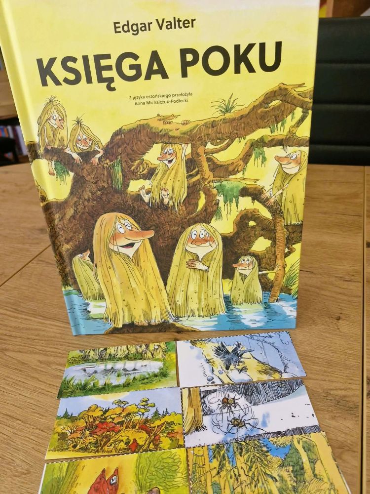 Na zdjęciu widoczna jest książka Księga Poku autorstwa Edgar Valter 📚 Okładka utrzymana jest w ciepłych, leśnych kolorach i przedstawia sympatyczne postacie Poku — małych, baśniowych istot ukrywających się pośród konarów drzew i mokradeł. Ilustracje mają charakter ręcznie rysowany, pełen humoru i przyrodniczego klimatu. Przed książką rozłożono kilka kart obrazkowych lub fragmentów ilustracji przedstawiających elementy natury: las, owady, ptaki, rośliny, krajobrazy przyrodnicze. Zdjęcie sugeruje wykorzystanie książki podczas: zajęć bibliotecznych, edukacji przyrodniczej, biblioterapii, warsztatów inspirowanych naturą i wyobraźnią 🌿 Całość tworzy przyjazny, bajkowy klimat zachęcający dzieci do odkrywania świata przyrody i literatury.